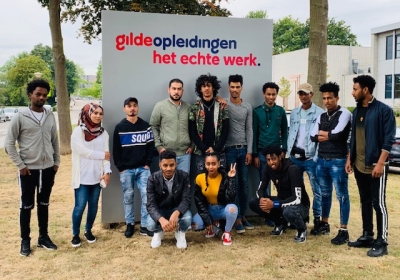 leerlingen voor bord met logo gilde opleidingen het echte werk