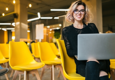 Vrouw zit in zaaltje met laptop op schoot